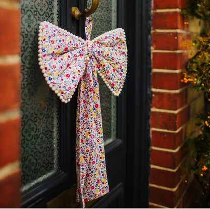A large decorative ditzy floral bow with mini pom pom trim and a ribbon hang tie