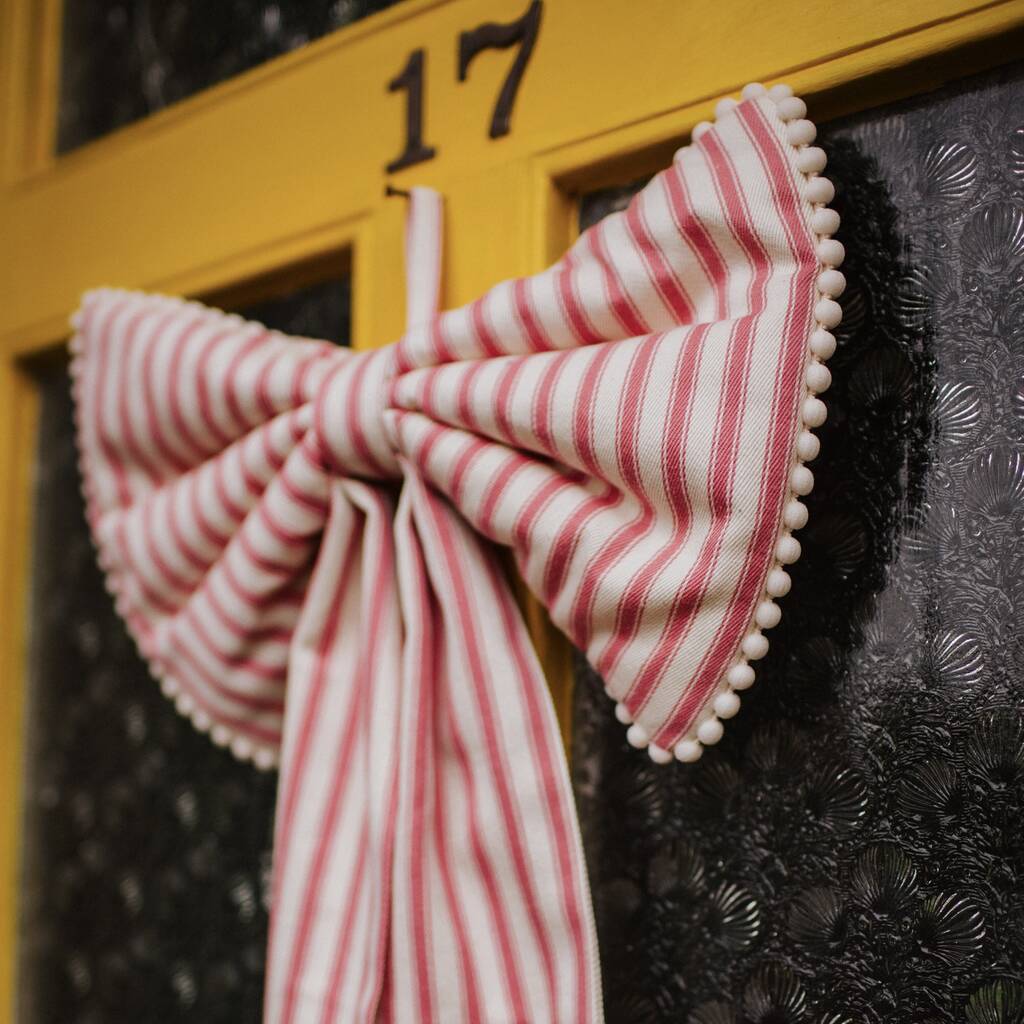 A large decorative pink stripe bow with mini pom pom trim and a ribbon hang tie