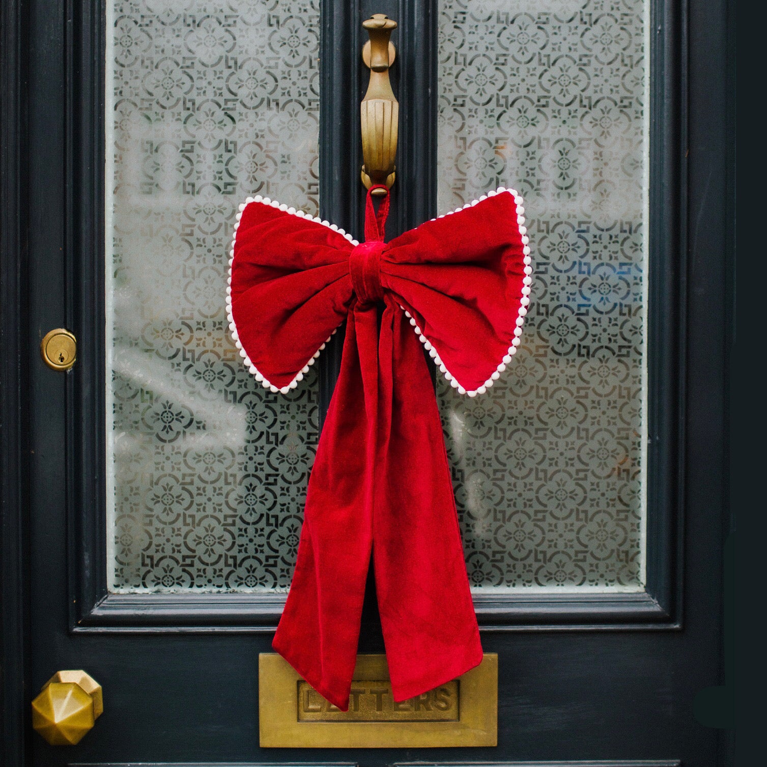 A large decorative red Christmas bow with mini pom pom trim and a ribbon hang tie